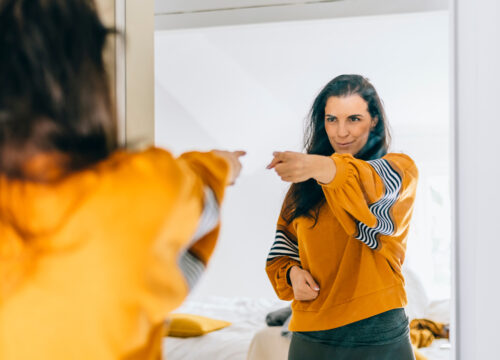 Self confident single woman pointing finger at reflection in mirror dancing and felling good.