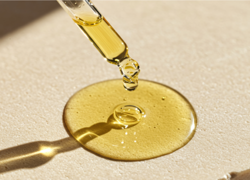 A glass dropper dispensing a concentrated golden peptide serum under bright sunlight, highlighting the use of peptides for skin repair and anti-aging in professional treatments.